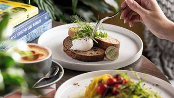 Un plato con una rebanada de pan cubierta de crema y vegetales, una cuchara, y un libro titulado "Hiking Alone Around the World" al fondo.