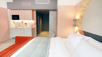 Ein modernes Hotelzimmer mit Bett, einer kleinen Küchenzeile und einem Badezimmer.