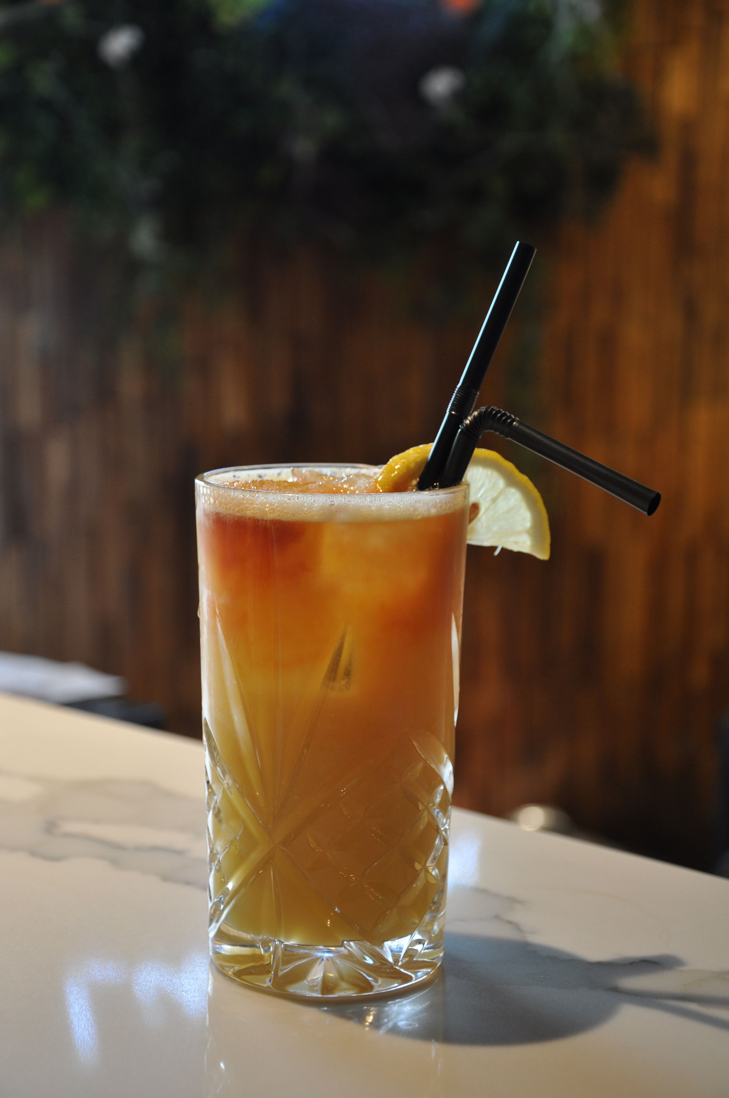 A tall glass with a lemon slice and two straws, placed on a table.