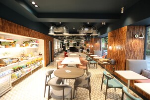 A modern cafe with a central table, seating around it, and a variety of food items on shelves.