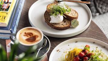 Une table à manger avec une assiette de bruschettas garnies de mozzarella et de verdure, une tasse de café et un livre.