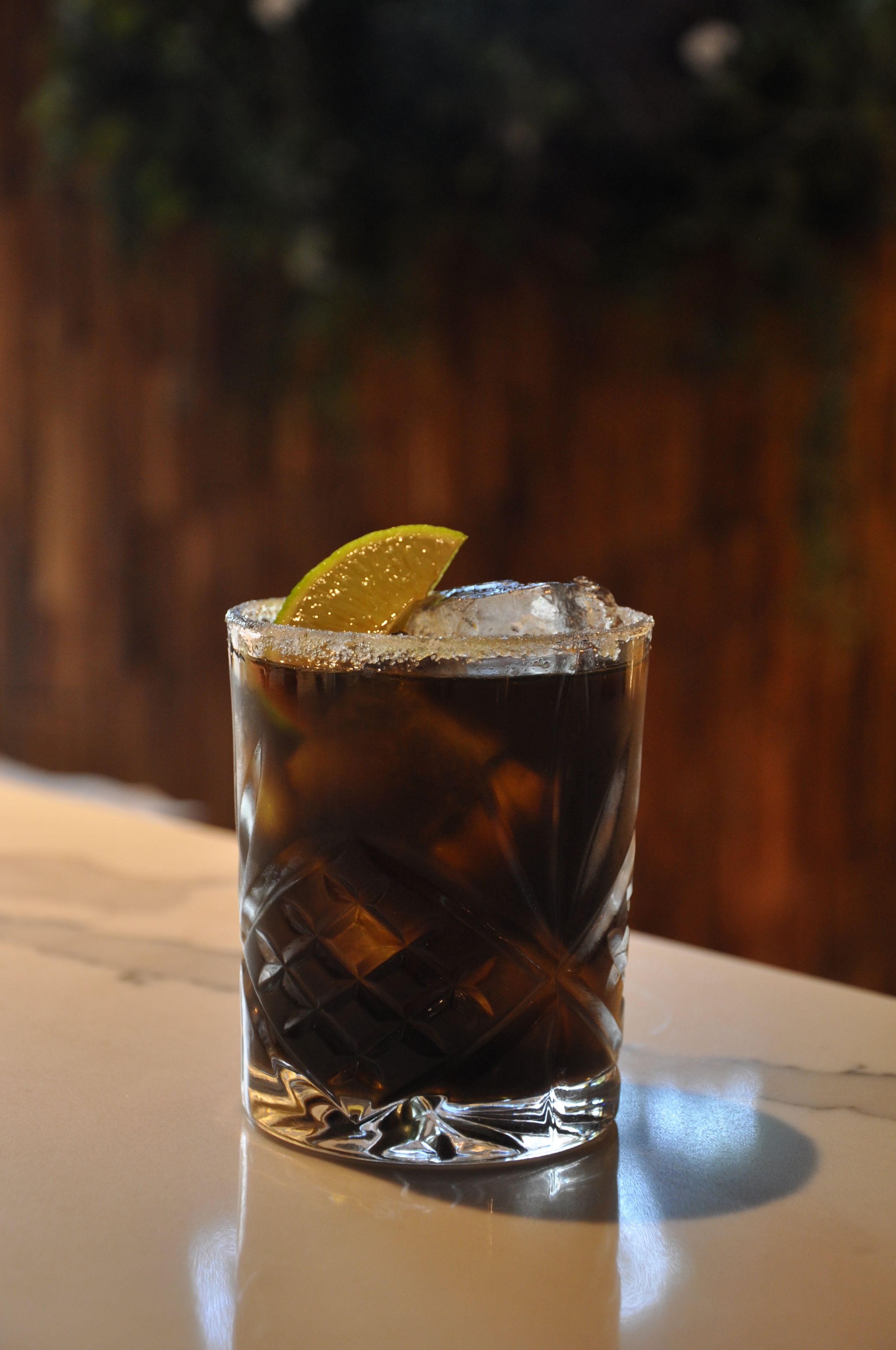 A glass of iced beverage with a lime wedge on a reflective surface.