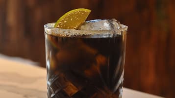 A glass of iced beverage with a lime wedge on a reflective surface.