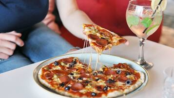Une pizza garnie de pepperoni et d’olives, présentée sur une assiette, un verre contenant une boisson avec une paille, et une part de pizza en train d’être soulevée.
