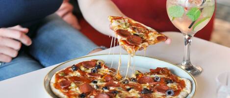 A pizza with pepperoni and olives on a plate, a glass of drink with a straw, and a slice being lifted.
