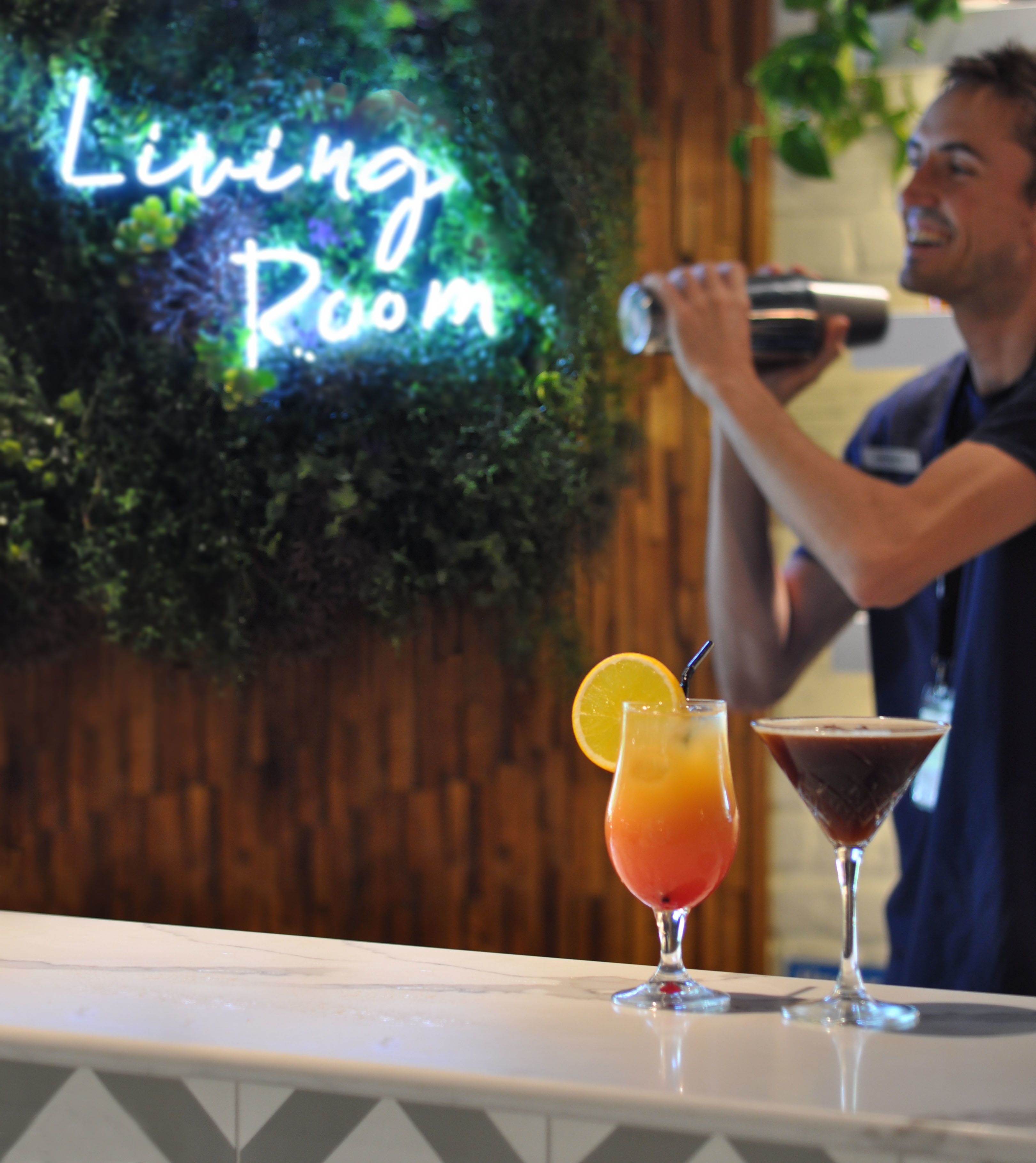 Zona de bar con un letrero de neón que dice "Living Room" y dos cócteles en la barra.