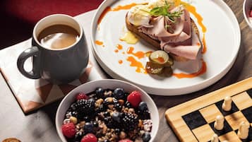 Una colazione con un piatto di cibo, una tazza di caffè, una ciotola di frutta e una scacchiera.