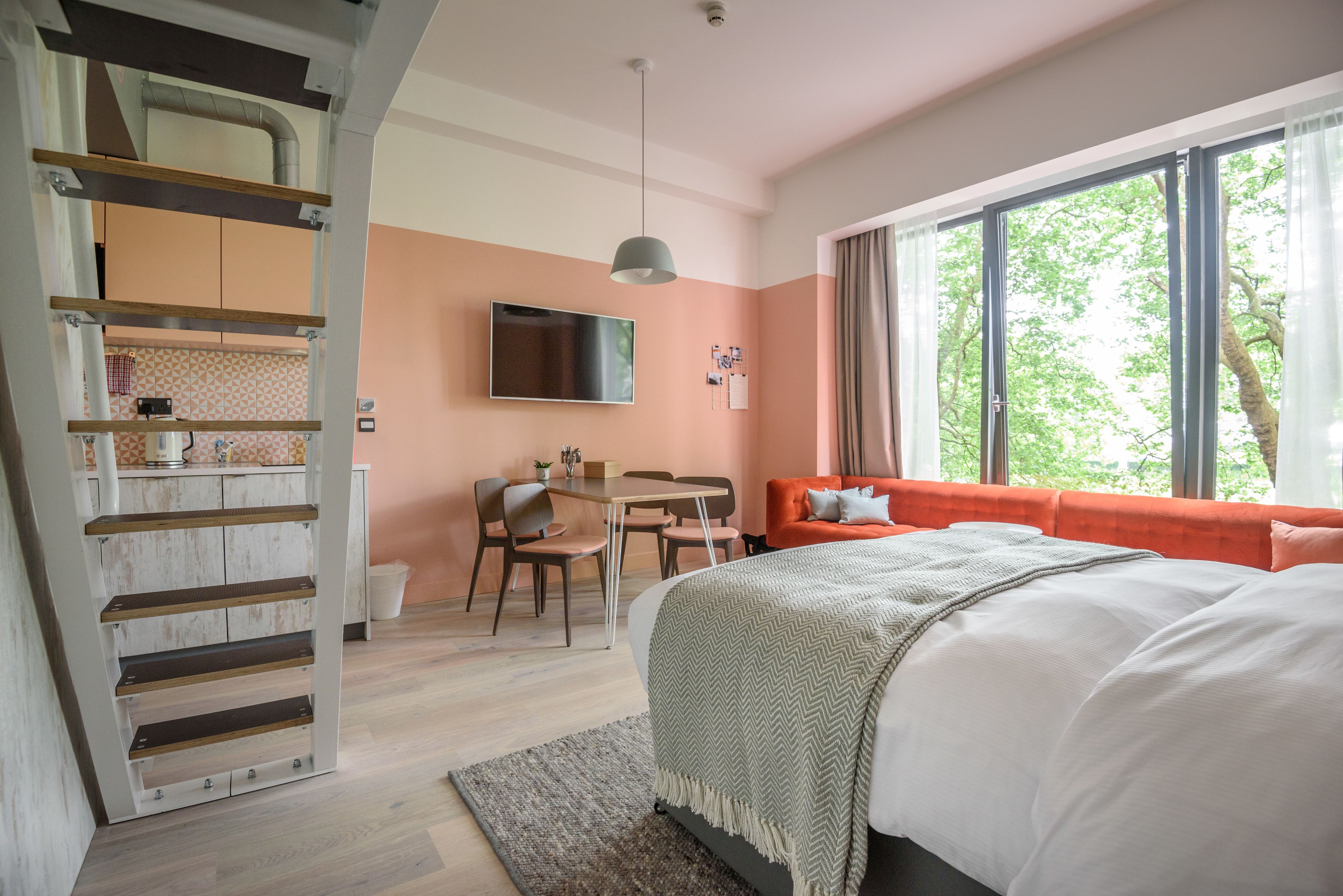 A modern bedroom with a bed, a desk, a chair, and a TV.