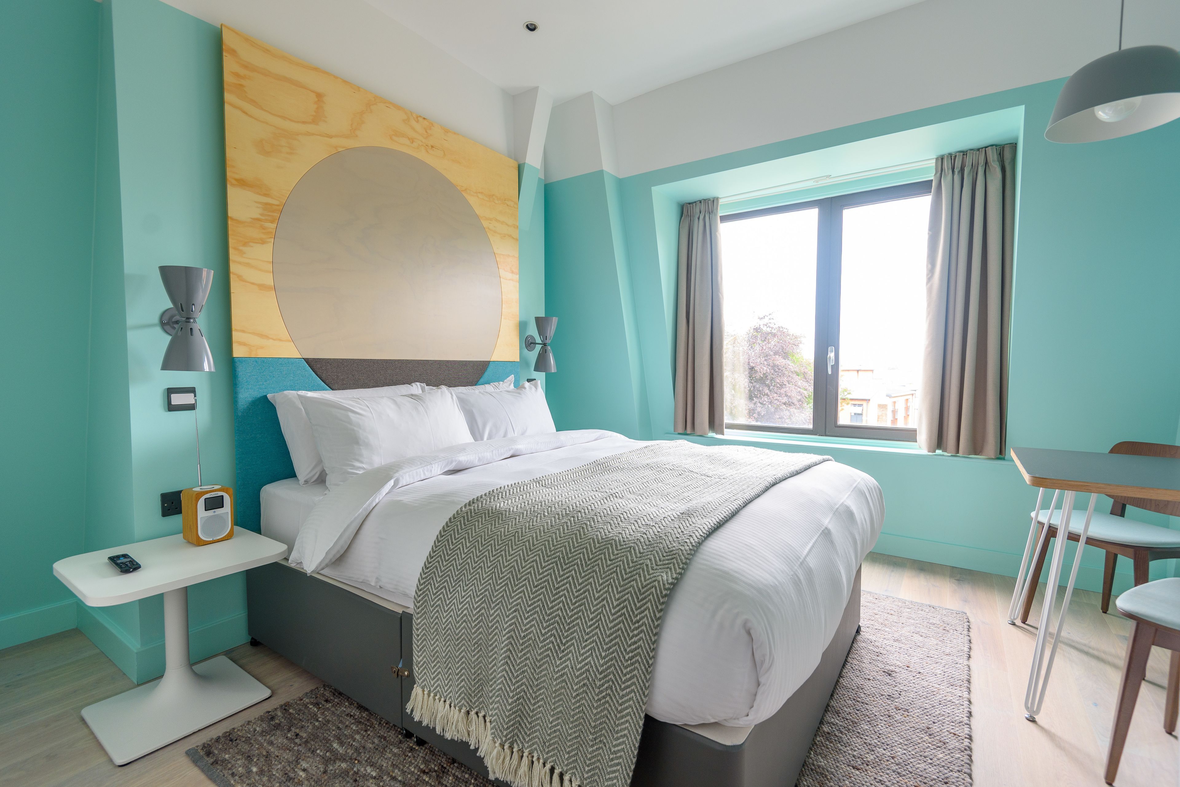 A modern bedroom with a bed, bedside table, and a window with curtains.