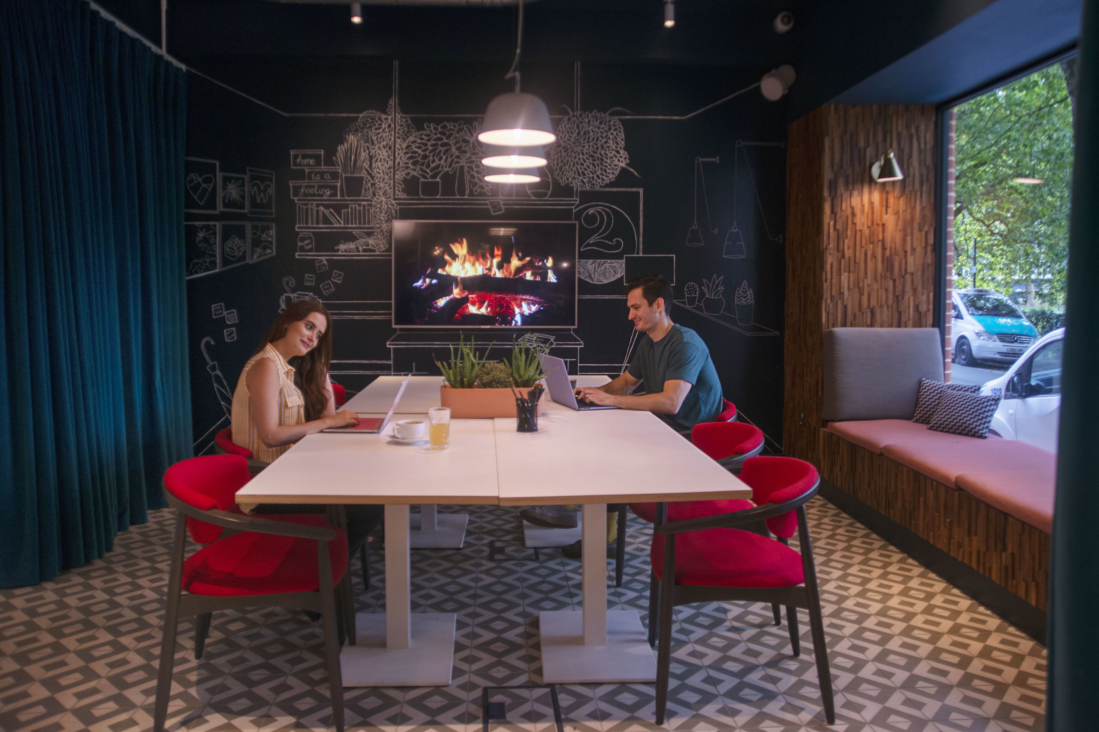 A modern meeting room with a large TV, red chairs, a white table, and a wooden accent wall.