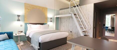 Ein modernes Hotelzimmer mit Bett, Schreibtisch, Stuhl, kleinem Tisch und einer Treppe.