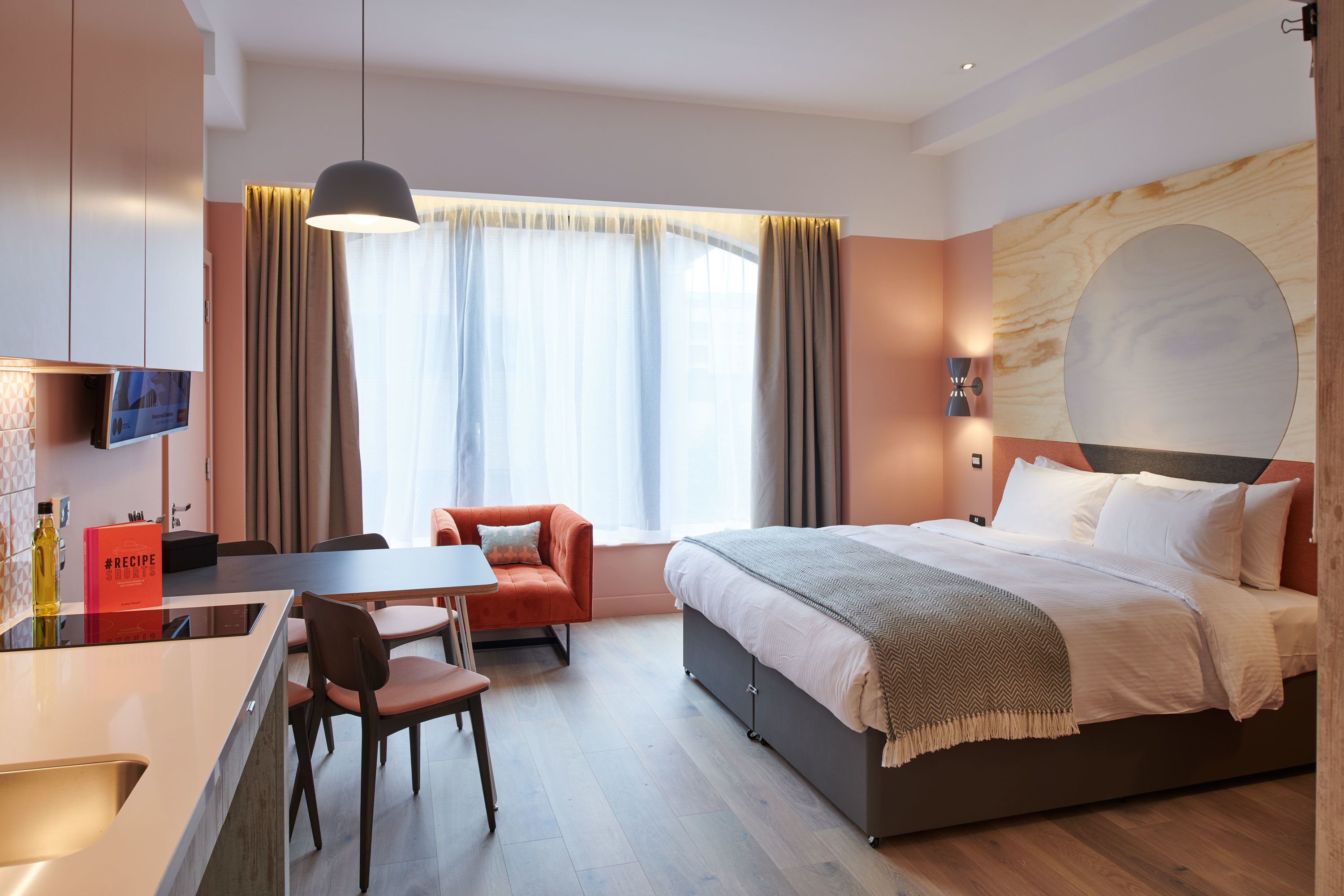 A modern hotel room with a bed, a desk, a chair, and a television.