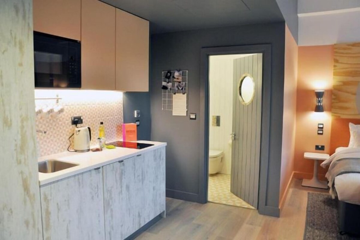 A compact hotel room with a kitchenette, a bathroom, and a bed.