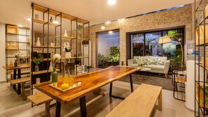 A modern interior with a wooden dining table, benches, and a sofa. There are shelves with decorative items and a large window with a view of the outdoors. - La Regatta Boutique Residences (Ho Chi Minh City)