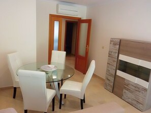 Un comedor con una mesa de vidrio y sillas blancas, un mueble de madera y una puerta que da a otra habitación.