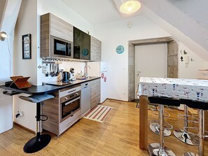 Een compacte keuken met moderne apparaten, een eethoek met een tafel en stoelen, en een zichtbare deur naar een andere kamer.
