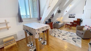 Un loft spacieux avec un plafond haut, un coin repas avec une table recouverte d’une nappe à motifs, un canapé et un tapis à motifs géométriques.