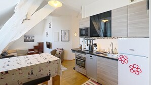 Une cuisine compacte dotée d’appareils électroménagers modernes, un coin repas avec une nappe à motifs et un espace salon confortable.