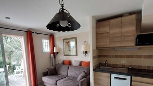 Un espace de vie compact comprenant un canapé, une table à manger, un coin cuisine et une porte-fenêtre coulissante donnant sur un espace extérieur.