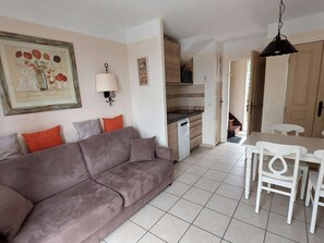 Una sala de estar con sofá, una mesa de comedor con sillas, una cocina equipada con lavavajillas y un pasillo que conduce a otra habitación.