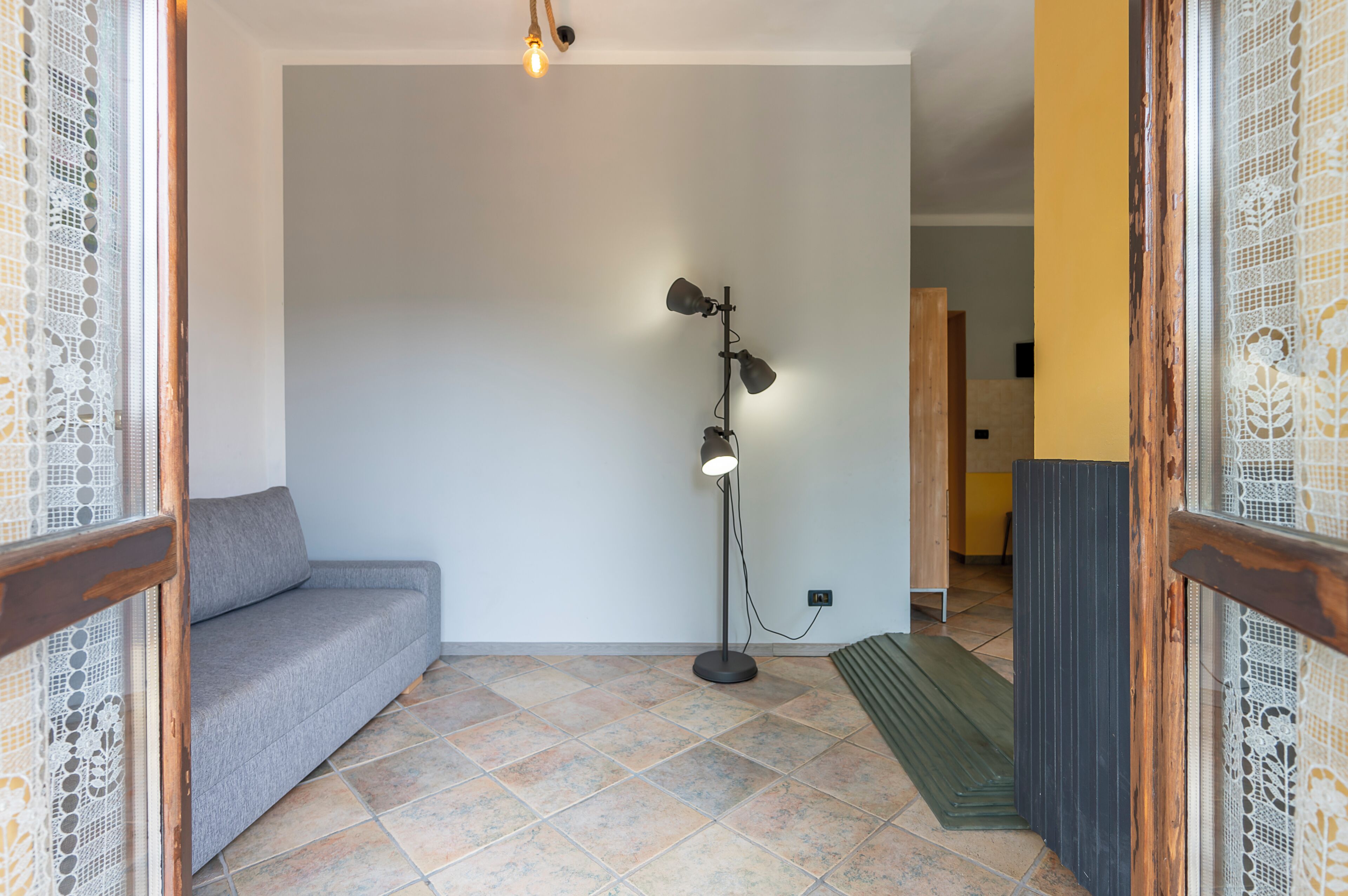 Ein Zimmer mit einer grauen Couch, einer Stehlampe und einem hölzernen Türrahmen.