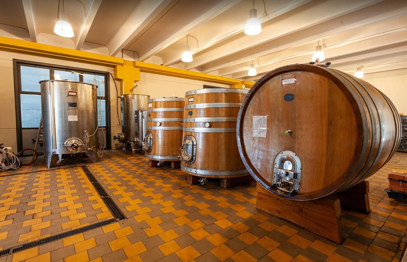 Een ruime ruimte met grote houten vaten en roestvrijstalen tanks, waarschijnlijk gebruikt voor opslag of fermentatie.