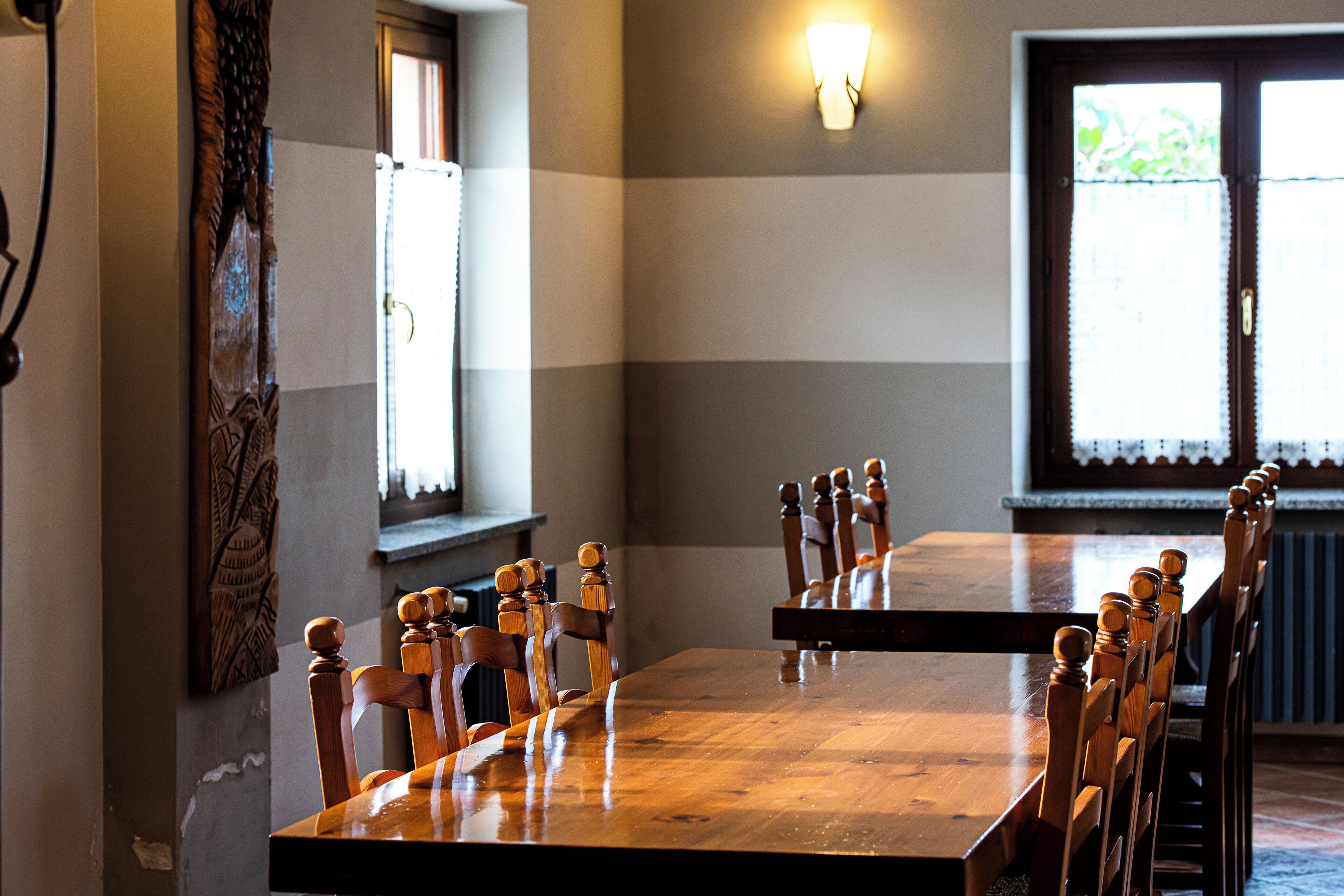 Une salle de conférence avec une longue table en bois et des chaises, un luminaire fixé au mur et des fenêtres équipées de stores.