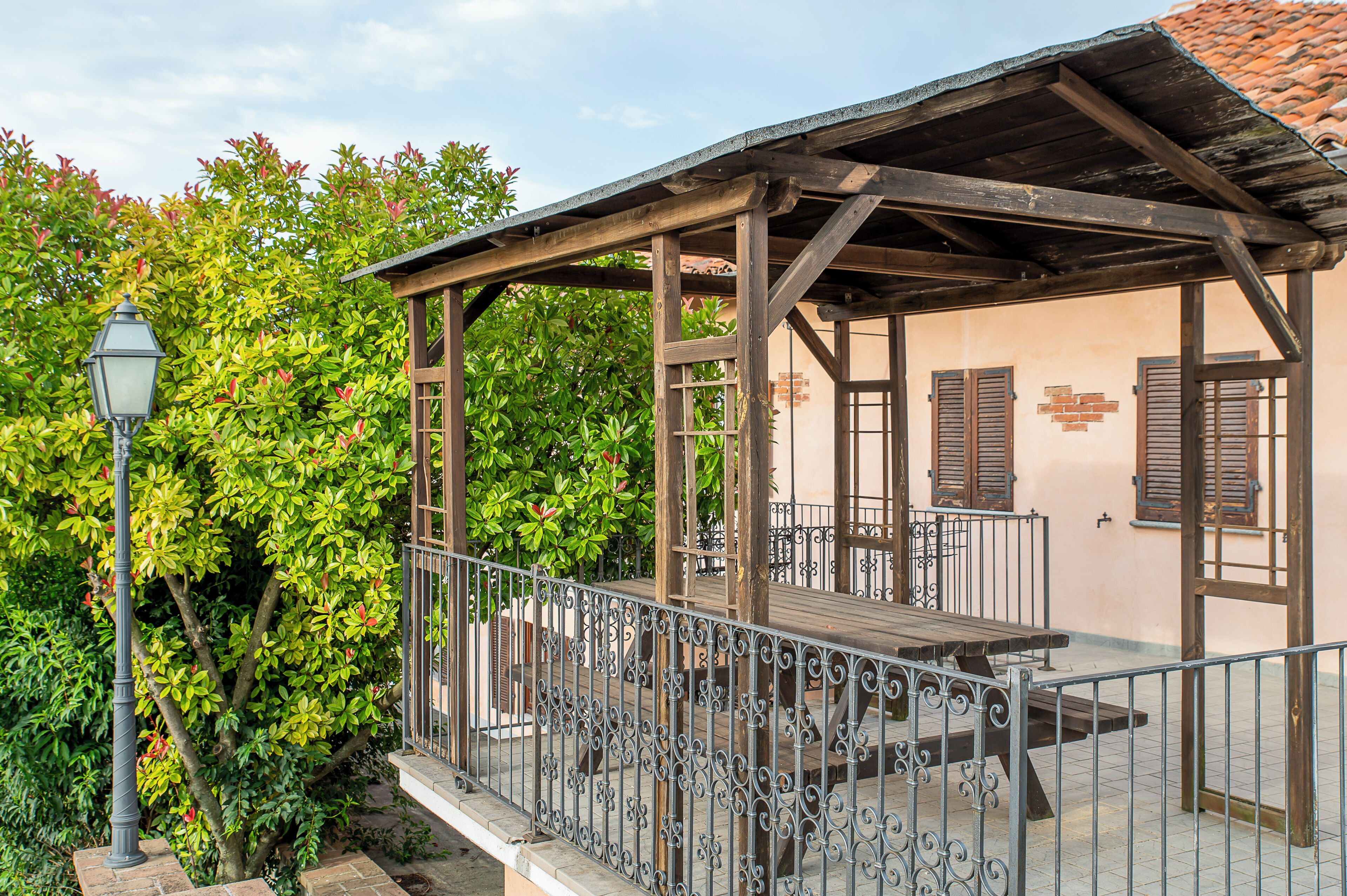 A covered outdoor seating area with a wooden pergola, metal railing, and a table.