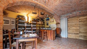 Une cave à vin aux murs de briques, avec des tables et des chaises en bois, des étagères remplies de bouteilles de vin et un comptoir en bois rustique.