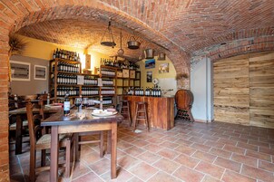 Una bodega de ladrillo con mesas y sillas de madera, estantes llenos de botellas de vino y un mostrador de madera rústico.