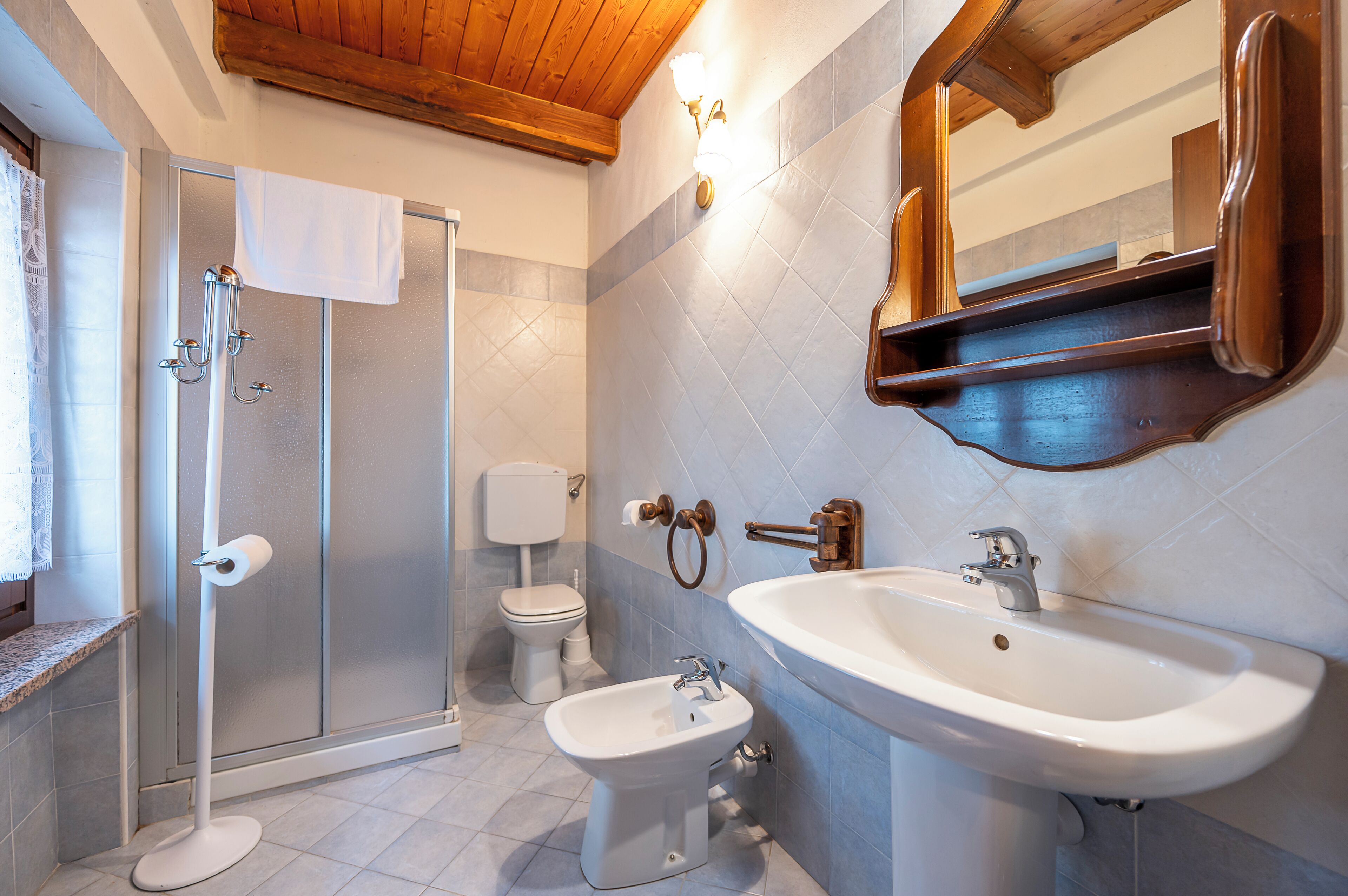 Ein Badezimmer mit Dusche, Toilette, Bidet, Waschbecken und einem spiegel mit Holzrahmen.