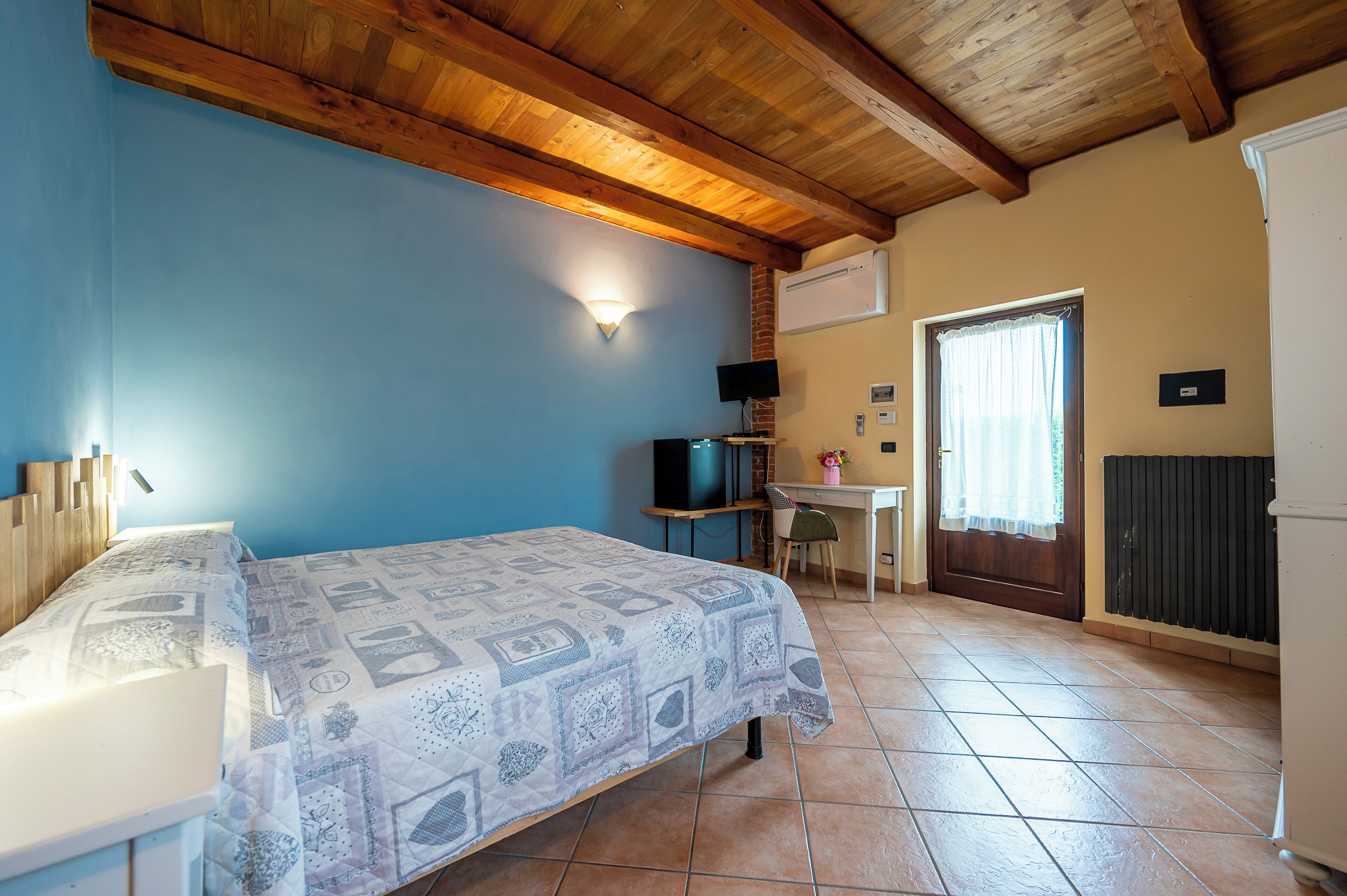 Een slaapkamer met een bed, een bureau, een stoel, een televisie en een deur met een raam.