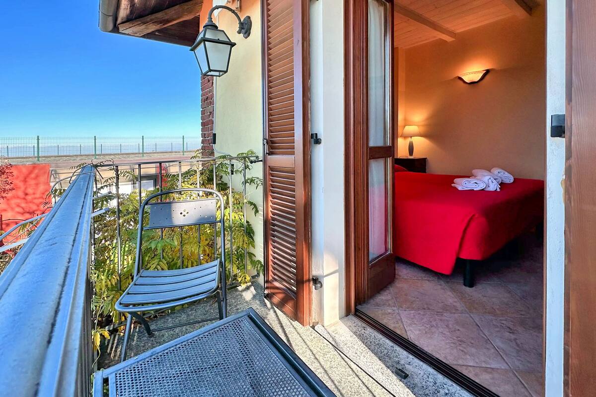 Een balkon met een metalen stoel, een klein tafeltje en een rode bed met witte handdoeken.
