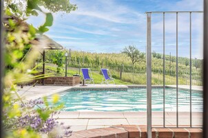 Una piscina con dos sillas reclinables azules, rodeada de una valla y follaje.