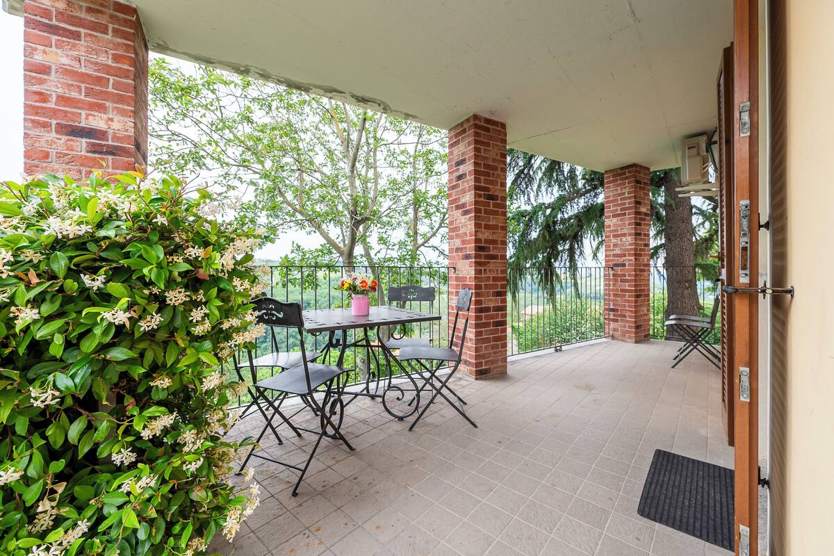 Een overdekt terras met een bakstenen pilaar, een tafel met stoelen en een potplant.