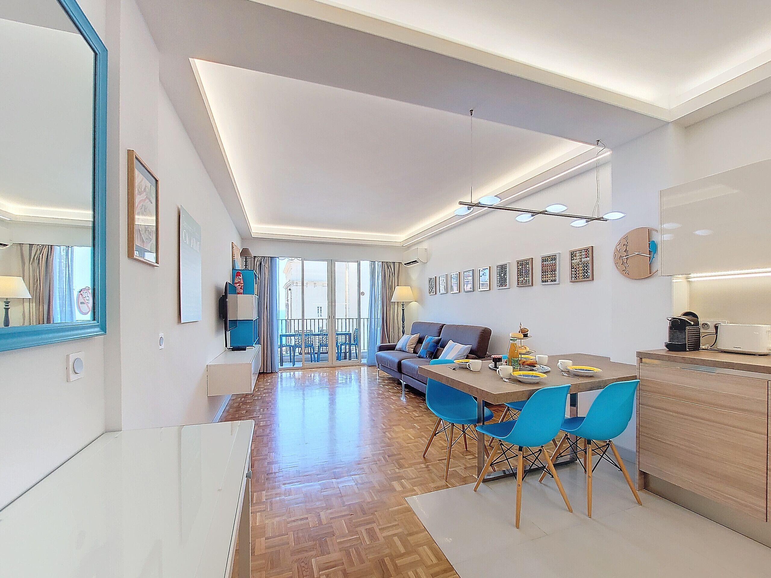 Un salon moderne comprenant un canapé, une table à manger avec des chaises, un coin cuisine et une grande fenêtre donnant sur l’extérieur.