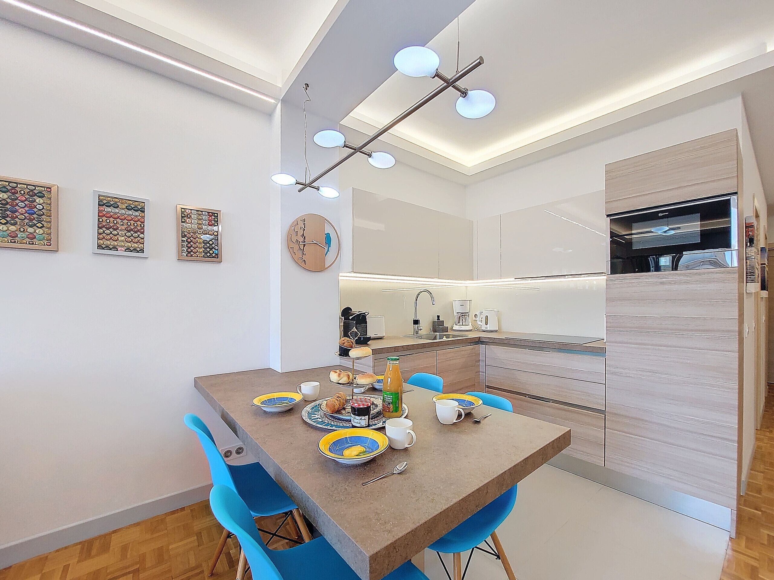 Un comedor moderno con una mesa de madera, sillas azules y una cocina al fondo.