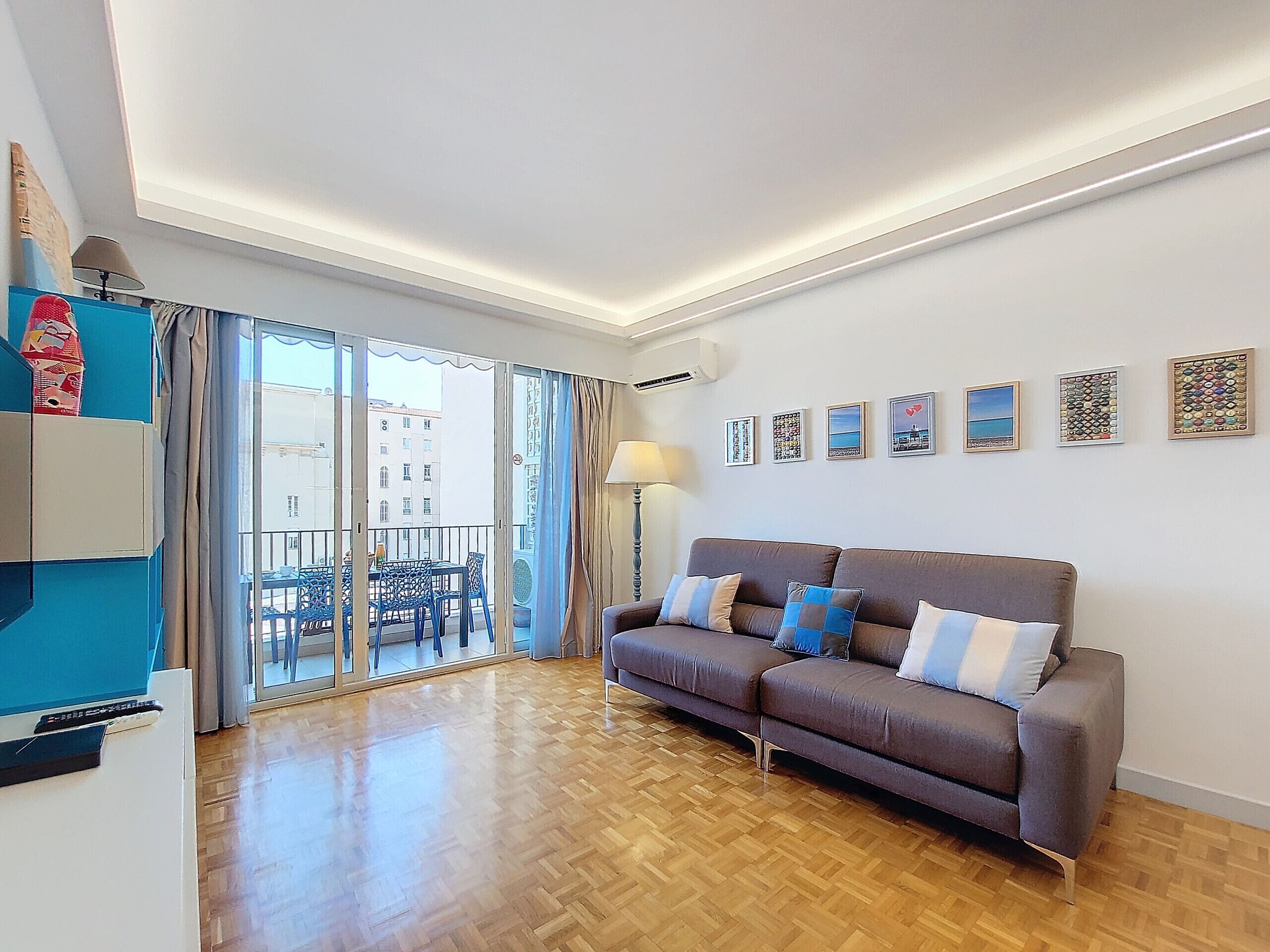 Una sala moderna con un sofá marrón, piso de madera y un balcón con sillas azules.