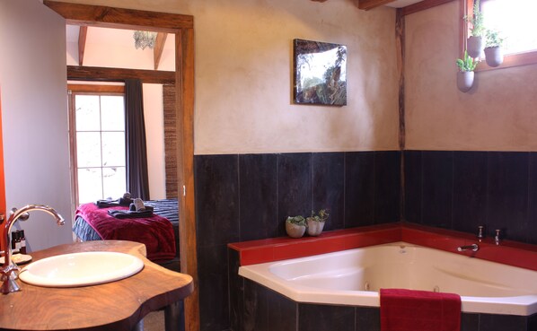 Een badkamer met een houten wastafel, een witte wasbak, een rode handdoek, een bad en een raam met planten.