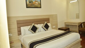 A neatly made bed with a headboard, two pillows, a bedside table, a chair, and a wall-mounted mirror. - Hotel Temple Inn (Amritsar)