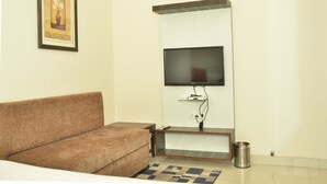 A living room with a brown sofa, a mounted TV, and a framed picture on the wall. - Hotel Temple Inn (Amritsar)