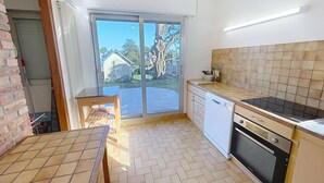 Une cuisine compacte avec une porte-fenêtre coulissante donnant sur un patio, un lave-vaisselle, un four et une petite table en bois.