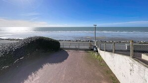 Un chemin pavé mène à une plage, bordée d’une clôture en métal et d’un lampadaire.