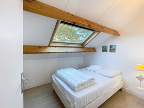 A bedroom with a skylight, a bed, a bedside table, and a lamp.