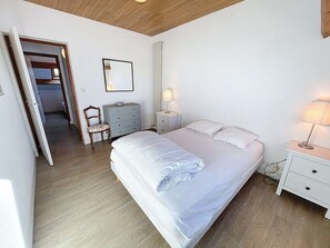 A bedroom with a large bed, a bedside table with a lamp, a dresser, a chair, and a mirror on the wall. - Seafront villa with garden and free Wifi (Saint-Pair-sur-Mer)