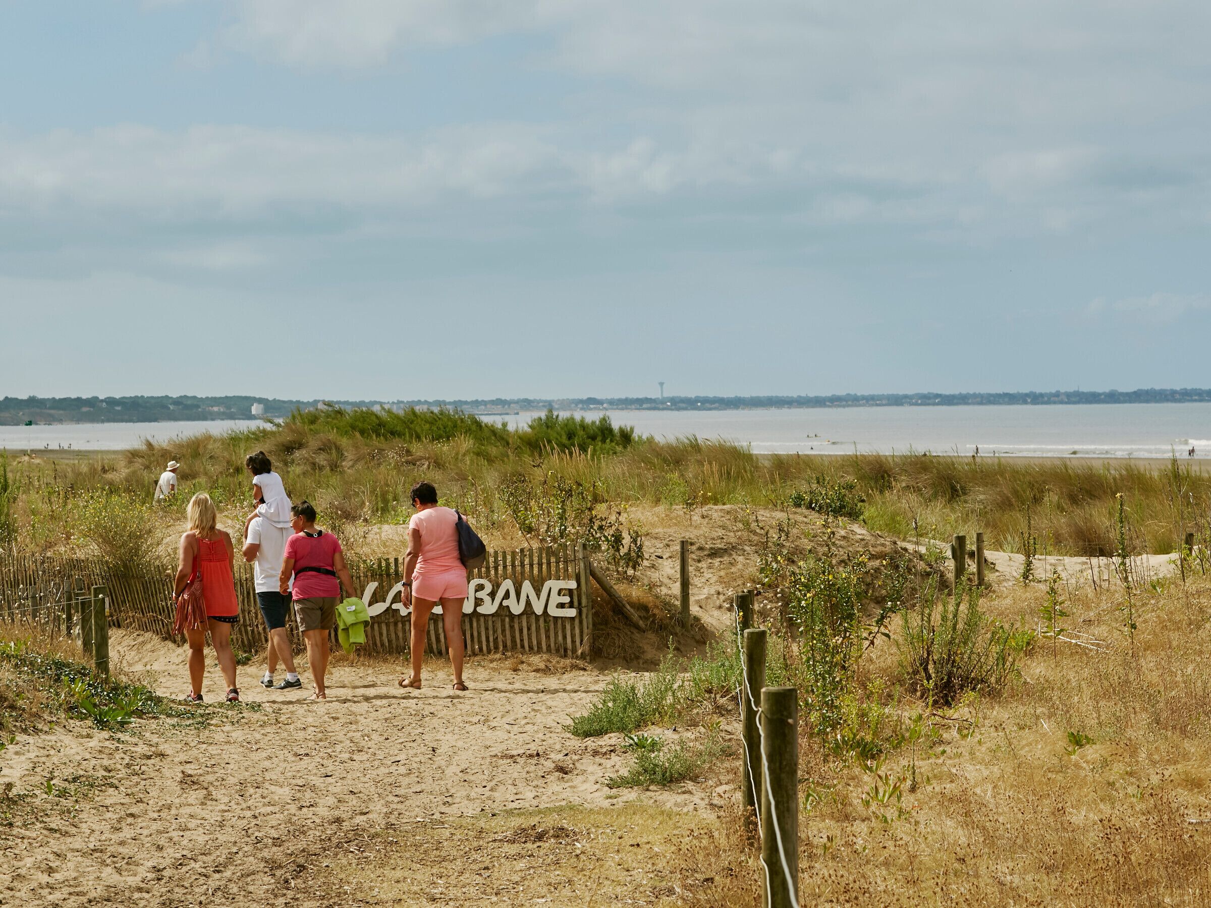 Un sentier de sable qui longe la plage et mène à un panneau sur lequel on peut lire « BANE ».