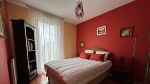 Quarto com uma cama grande, uma estante de livros e uma janela com cortinas.