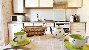Cozinha com armários brancos, micro-ondas, fogão e pia. Há pratos e xícaras verdes e brancos, além de uma cesta com croissants.