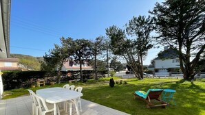 A patio with a tiled floor, a white table with chairs, and a small wooden table with a cushion. - Beachside Villa with Garden, Free Wifi & BBQ – Close to Shops & Attractions (Jullouville)