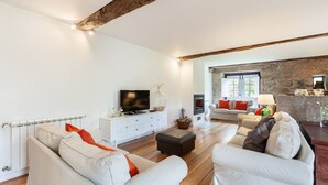 A modern living room with a fireplace, white sofas, a TV, and a stone wall. - Eido do Carvalhoso (Arcos de Valdevez)